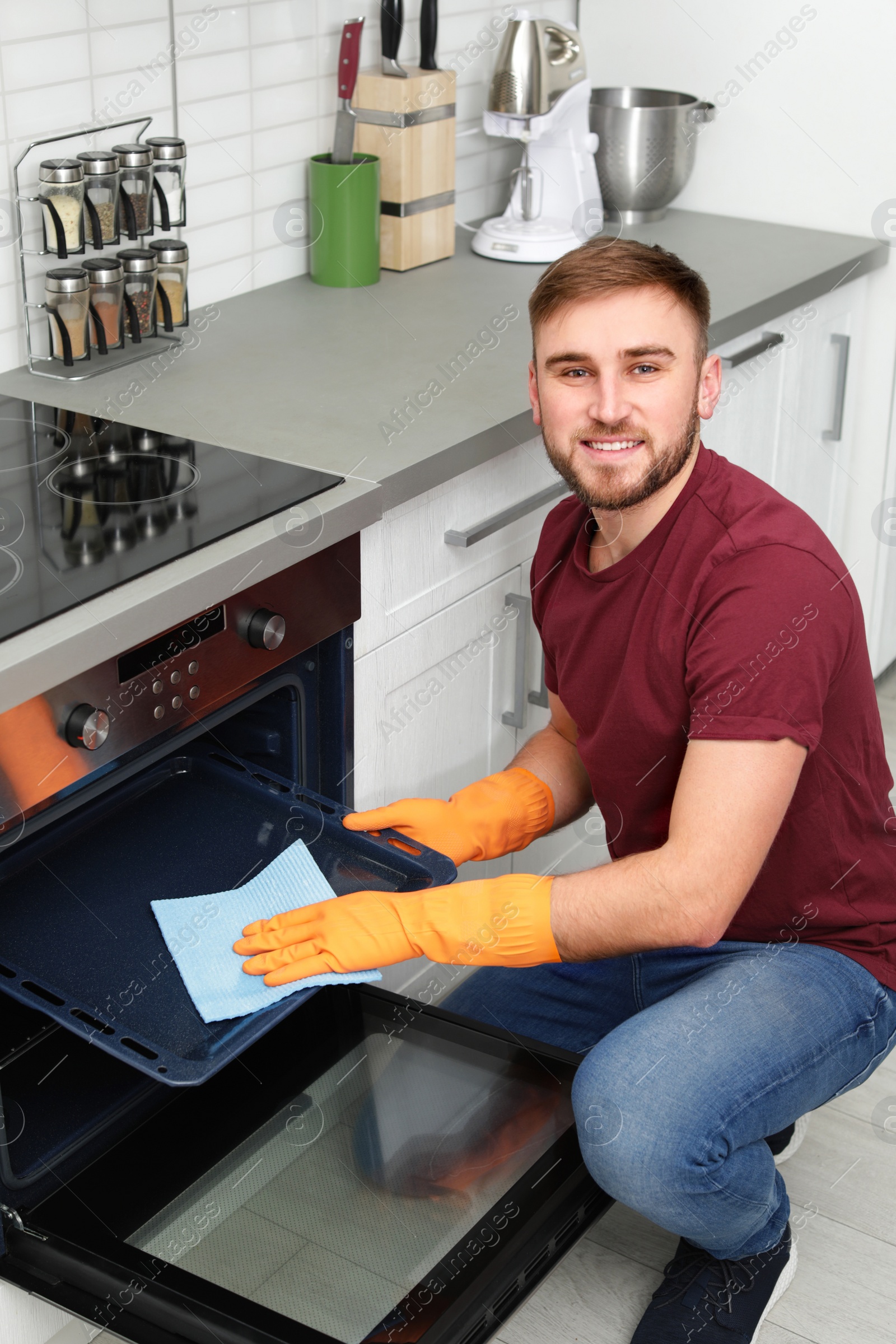 Photo of Young man cleaning oven tray with rag in kitchen