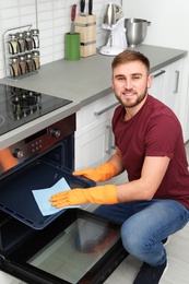 Young man cleaning oven tray with rag in kitchen