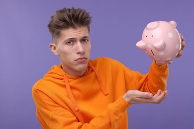 Upset man with piggy bank on purple background