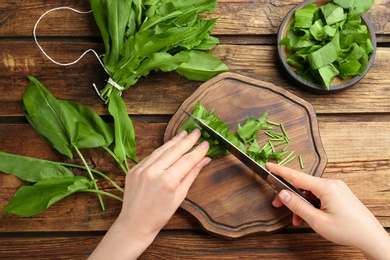 Photo of Woman cutting sorrel leaves at wooden table, top view