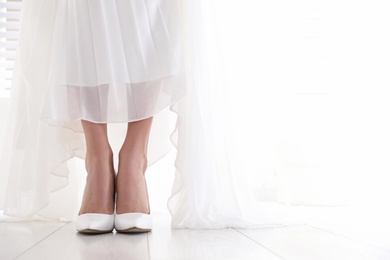 Photo of Young bride wearing beautiful wedding shoes indoors, closeup. Space for text