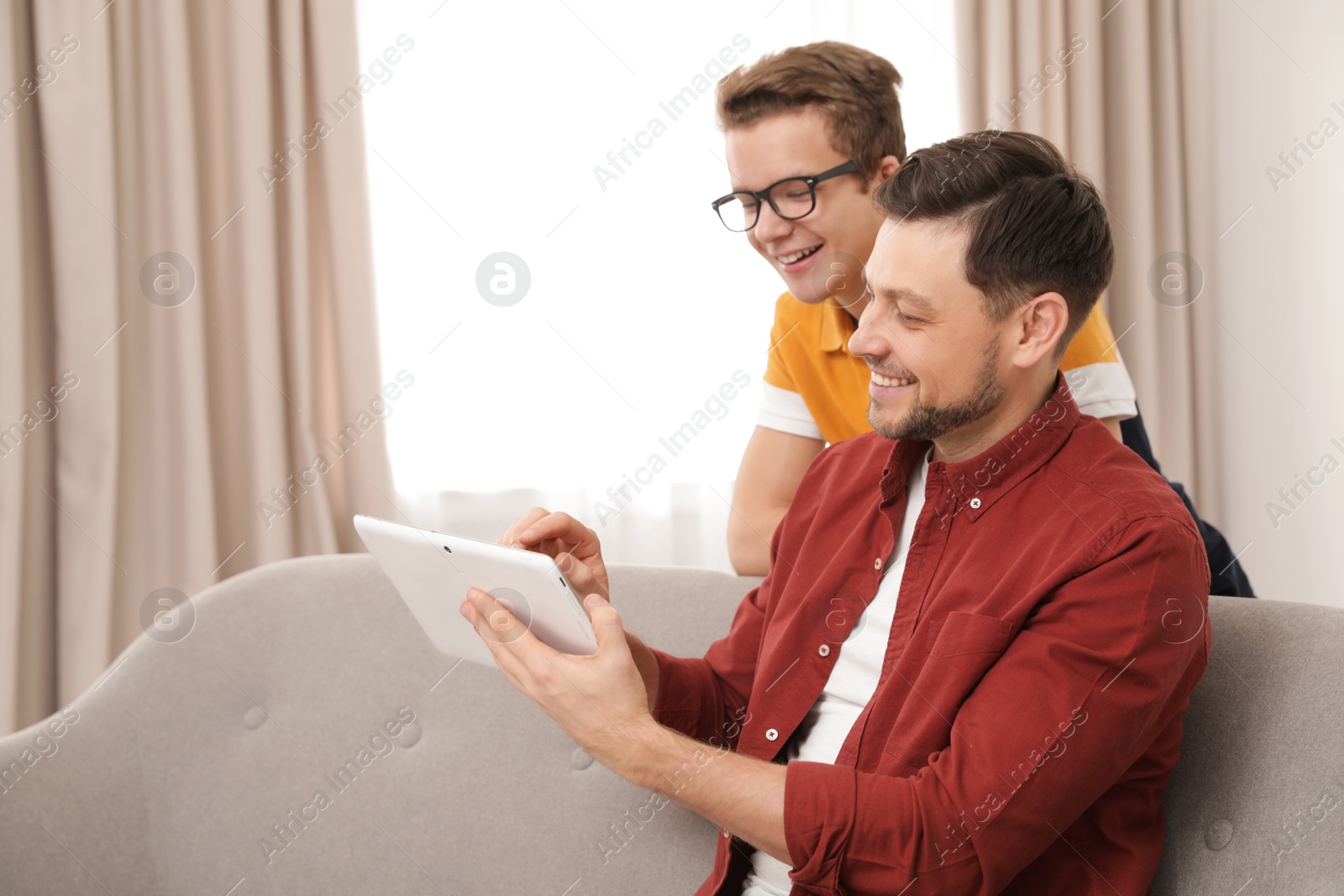 Photo of Happy father and his teenager son with tablet computer at home