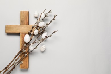 Wooden cross, painted Easter eggs and willow branches on light grey background, top view. Space for text