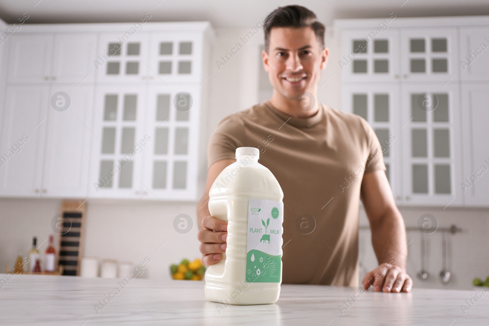 Image of Man with gallon bottle of vegan milk at white marble table in kitchen