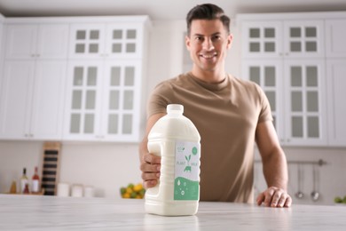 Image of Man with gallon bottle of vegan milk at white marble table in kitchen