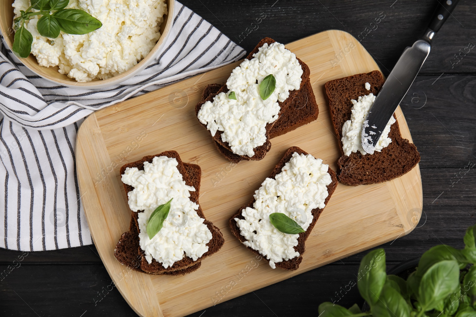 Photo of Bread with cottage cheese and basil on black wooden table, flat lay