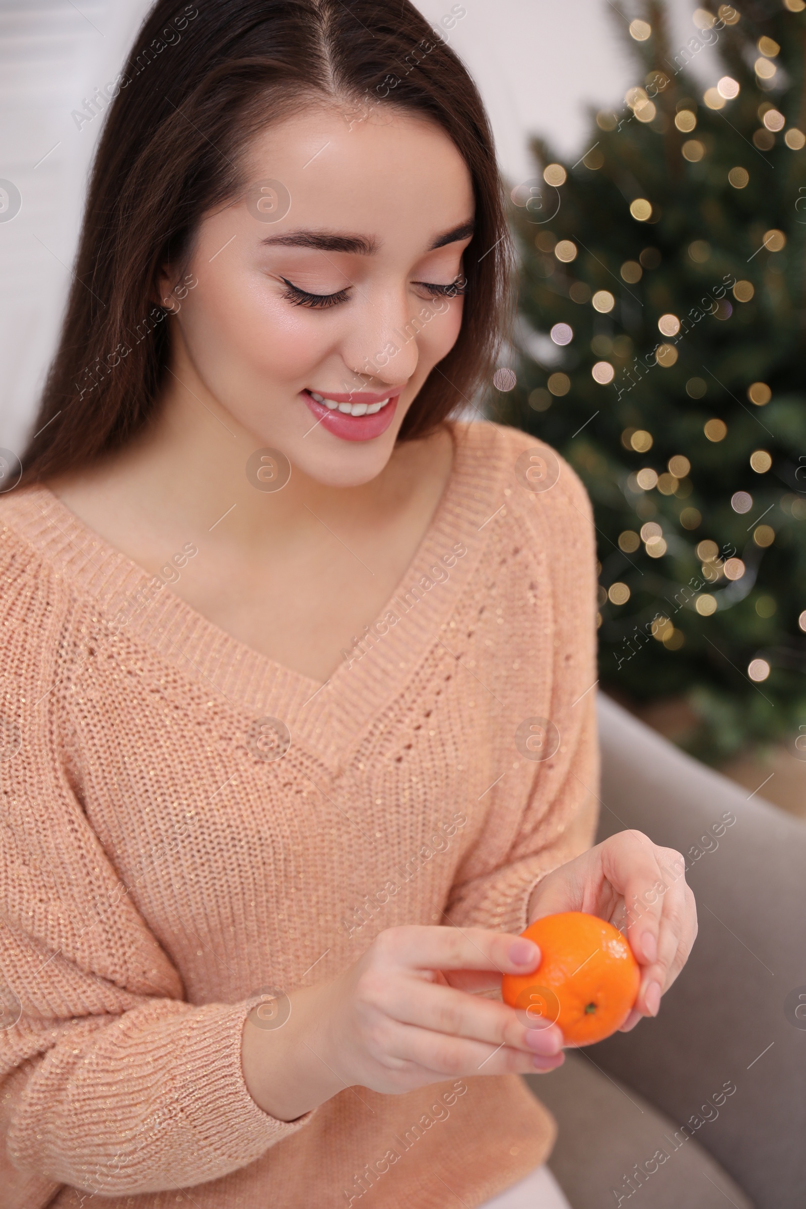 Photo of Happy young woman eating ripe tangerine at home