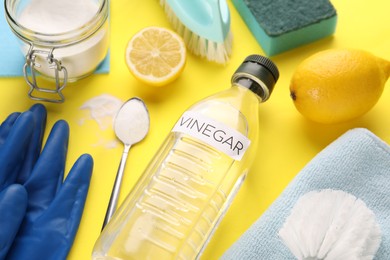 Photo of Eco friendly natural cleaners. Vinegar in bottle, soda, lemons and gloves on yellow background