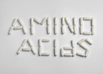 Photo of Phrase Amino acids made of pills on white background, flat lay