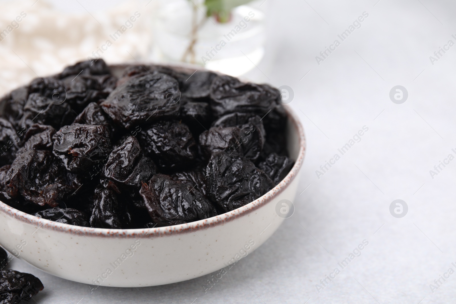 Photo of Sweet dried prunes in bowl on light table, closeup. Space for text