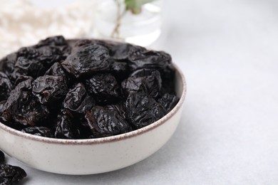 Sweet dried prunes in bowl on light table, closeup. Space for text