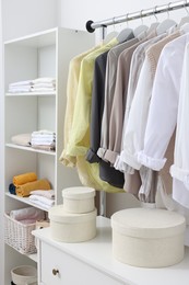 Photo of Wardrobe organization. Rack with different stylish clothes, shelving unit and chest of drawers indoors