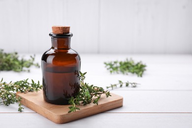 Photo of Bottle of thyme essential oil and fresh plant on white wooden table, space for text