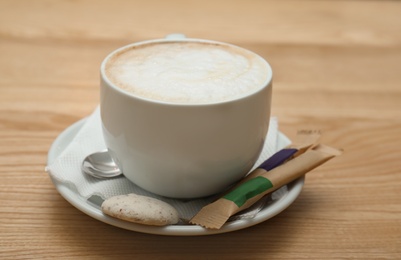Photo of Cup of aromatic cacao with sugar sticks and cookie on wooden table