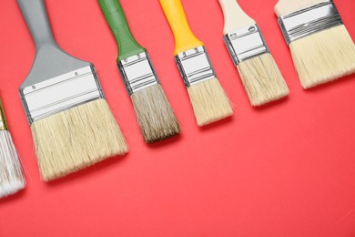 Photo of Many different paint brushes on red background, flat lay. Space for text