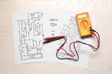 Photo of Wiring diagrams and digital multimeter on white wooden table, flat lay
