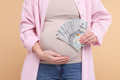 Photo of Surrogate mother. Pregnant woman with dollar banknotes on beige background, closeup