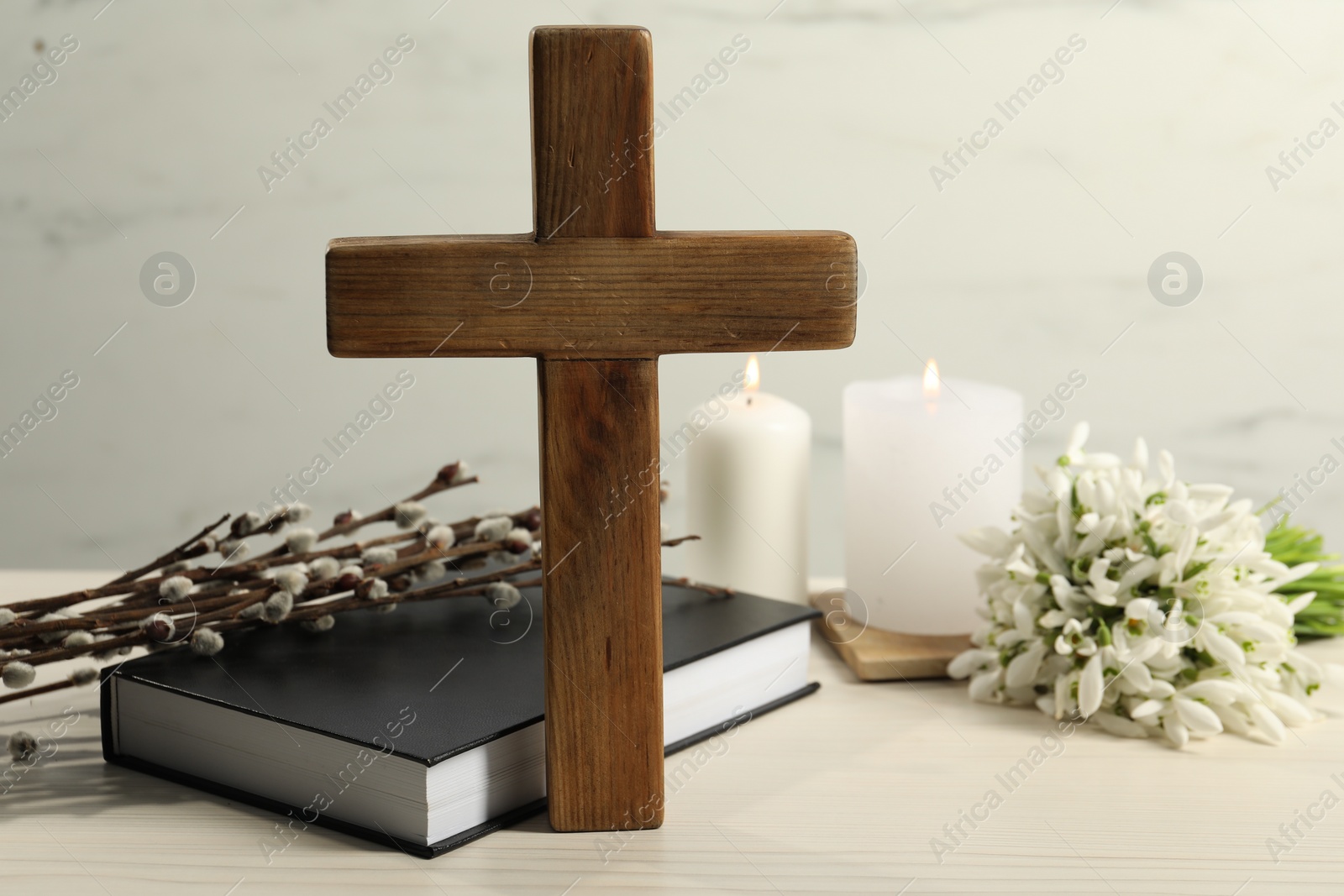 Photo of Wooden cross, Bible, church candles, willow branches and snowdrops on white table