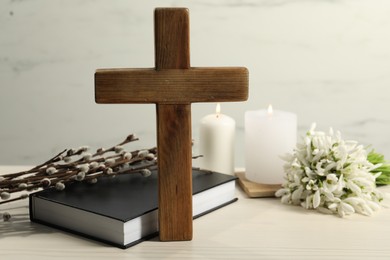 Photo of Wooden cross, Bible, church candles, willow branches and snowdrops on white table
