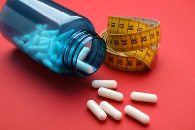 Photo of Jar of weight loss pills and measuring tape on red background, closeup