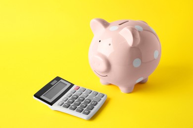 Photo of Calculator and pink piggy bank on yellow background