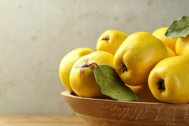 Photo of Tasty ripe quince fruits in wooden bowl on table, closeup. Space for text