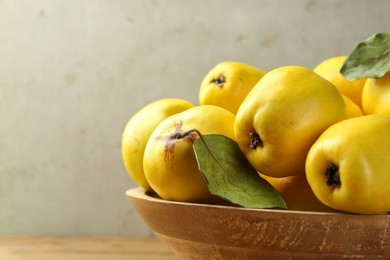 Tasty ripe quince fruits in wooden bowl on table, closeup. Space for text