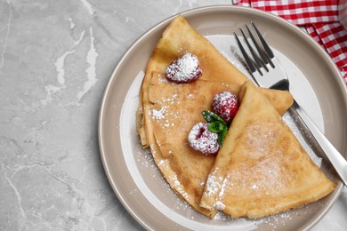 Photo of Delicious crepes served with mint, raspberries and powdered sugar on grey table, top view