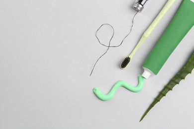 Photo of Tube of toothpaste, toothbrush, dental floss and fresh aloe on light grey background, flat lay. Space for text