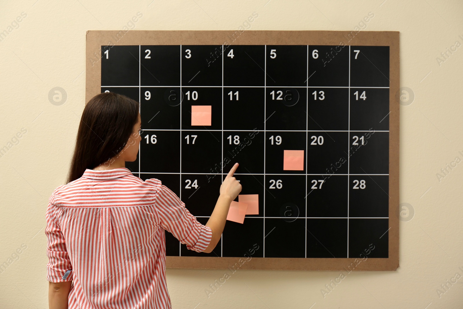 Photo of Young woman near board calendar  indoors, back view