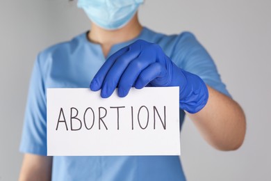 Photo of Doctor holding paper card with word ABORTION on light grey background, closeup