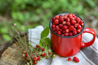 Photo of Mug and tasty wild strawberries on stump against blurred background, closeup