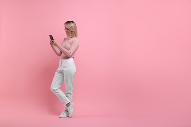 Happy woman with phone on pink background, space for text