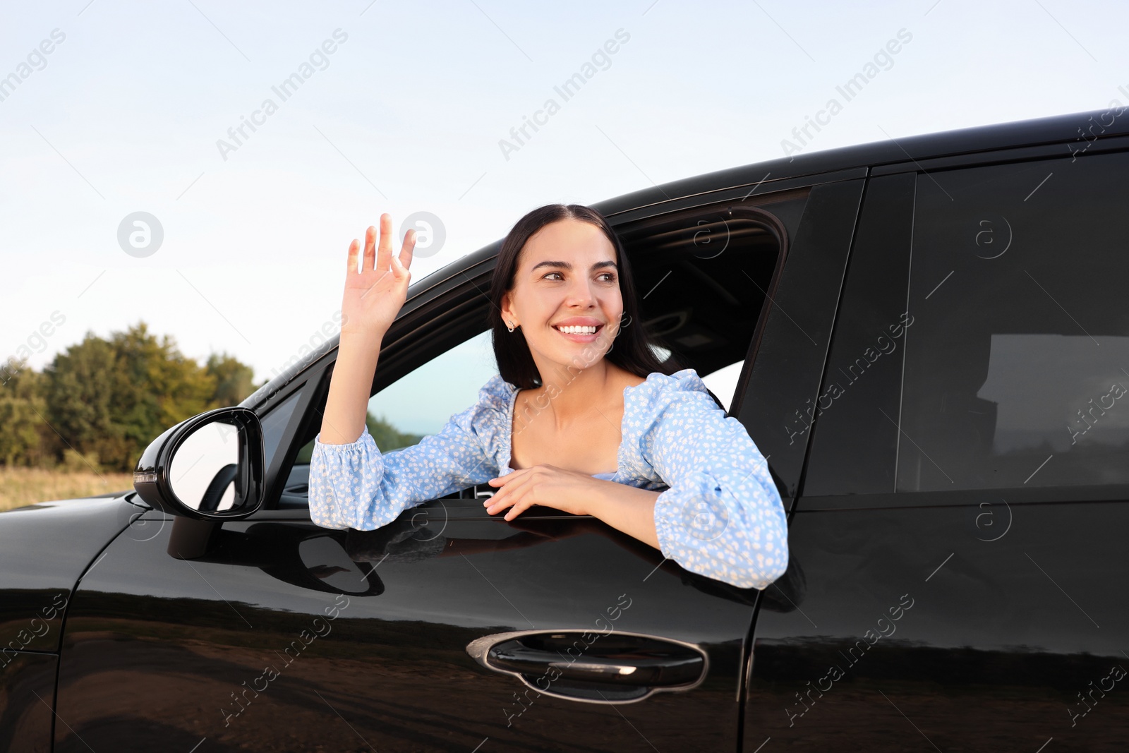 Photo of Enjoying trip. Portrait of beautiful happy woman waving in car, view from outside