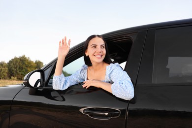 Photo of Enjoying trip. Portraitbeautiful happy woman waving in car, view from outside