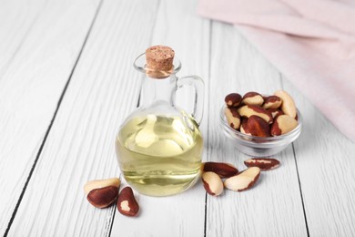 Photo of Tasty Brazil nuts and bottle with oil on white wooden table