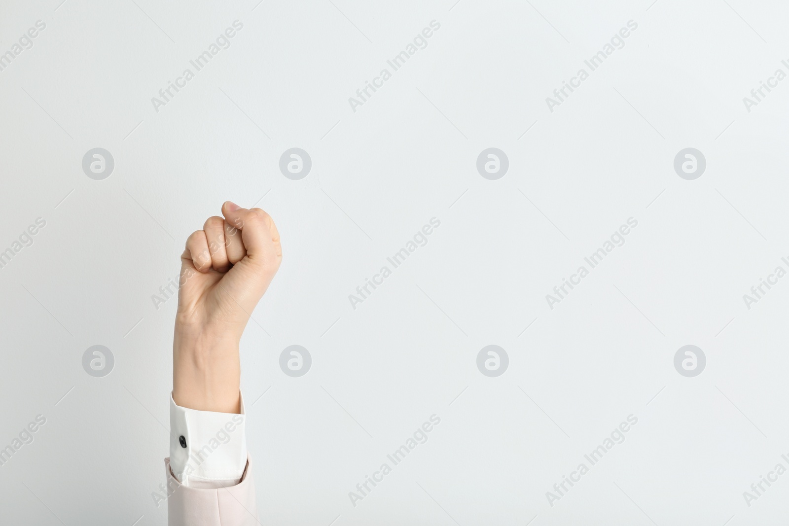 Photo of Young woman showing clenched fist on light background. Space for text