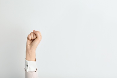 Photo of Young woman showing clenched fist on light background. Space for text