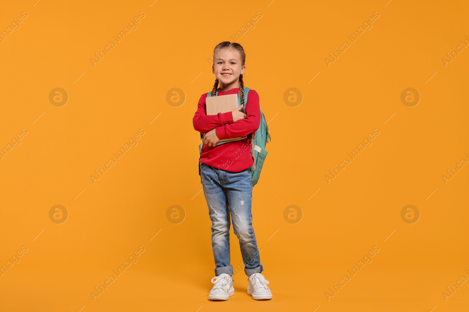 Photo of Happy schoolgirl with backpack and books on orange background