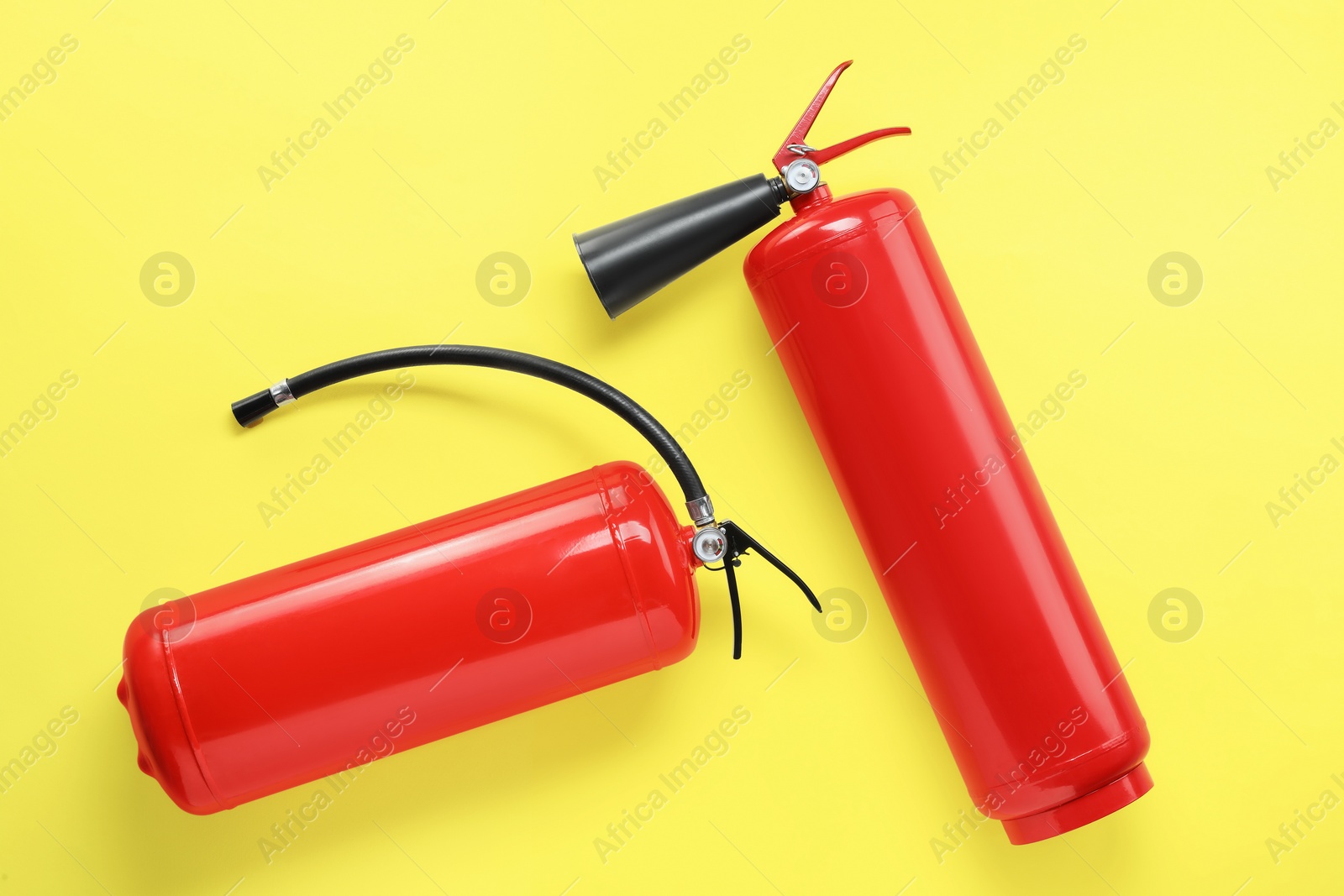 Photo of Two fire extinguishers on yellow background, flat lay