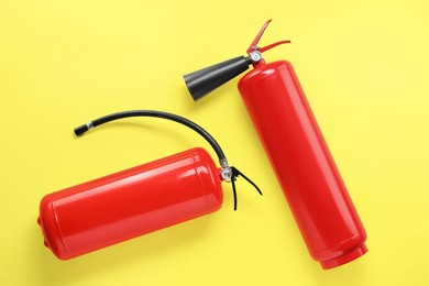 Photo of Two fire extinguishers on yellow background, flat lay