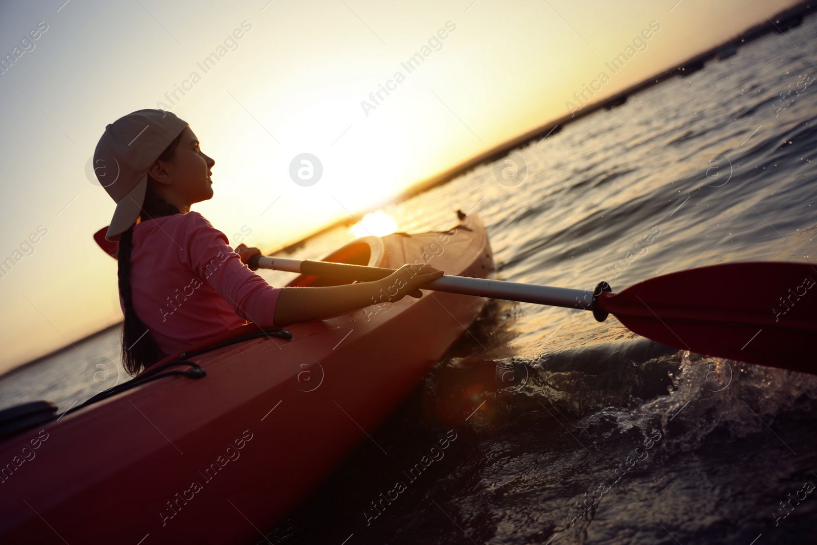 Photo of Little girl kayaking on river at sunset. Summer camp activity