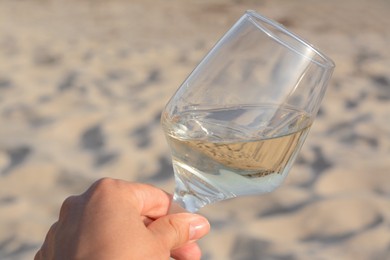 Woman holding glass of tasty wine on sand, closeup