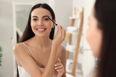 Photo of Beautiful young woman applying mascara near mirror in bathroom