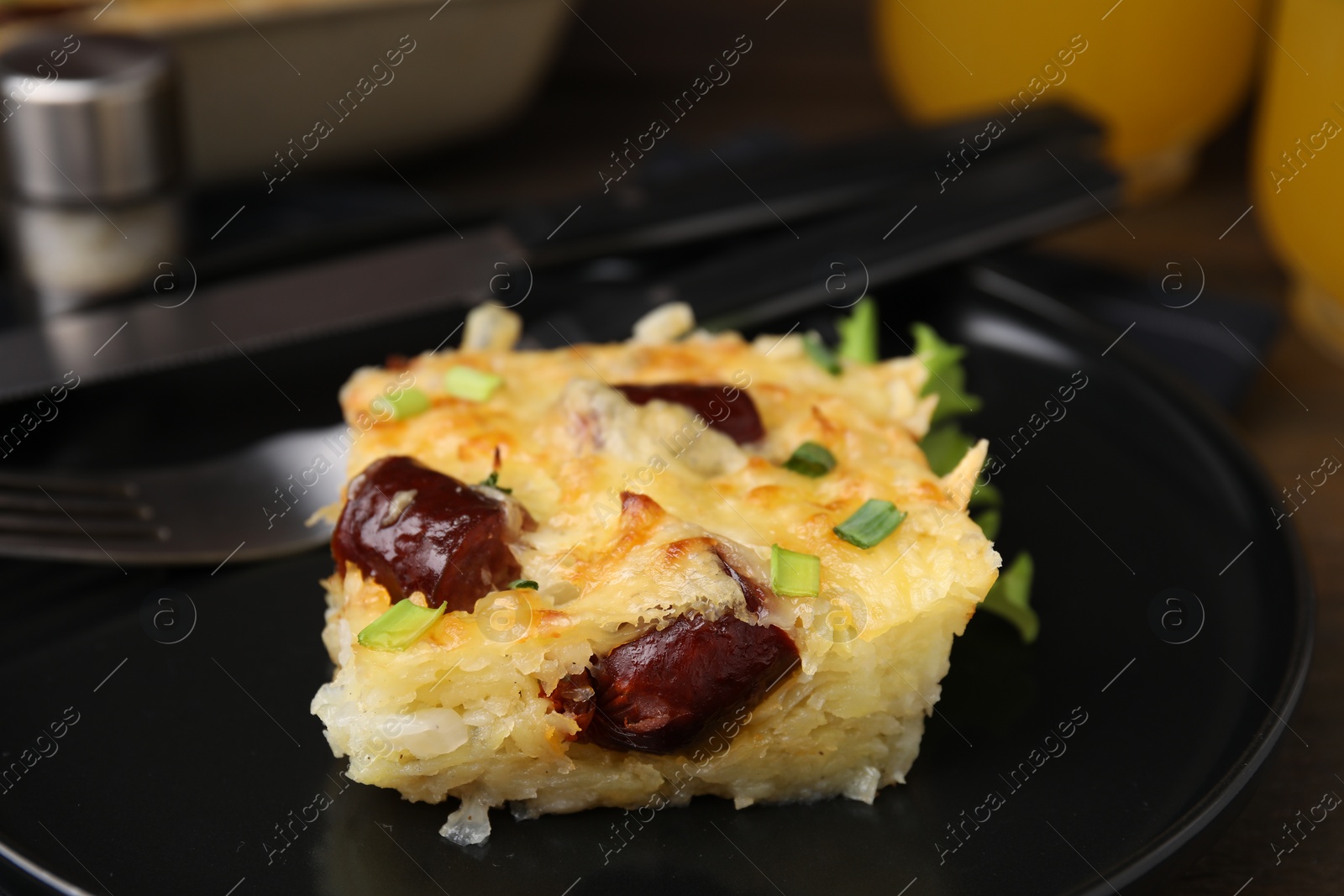 Photo of Tasty sausage casserole with green onions and cutlery served on table, closeup