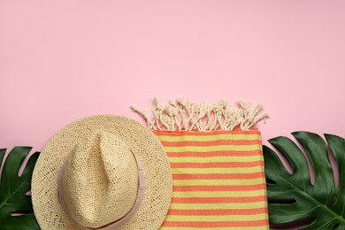 Beach towel and straw hat on pink background, flat lay. Space for text