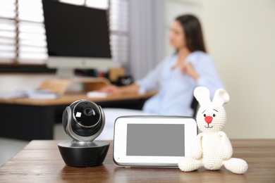 Photo of Baby monitor, camera with toy on table and woman working in home office. Video nanny