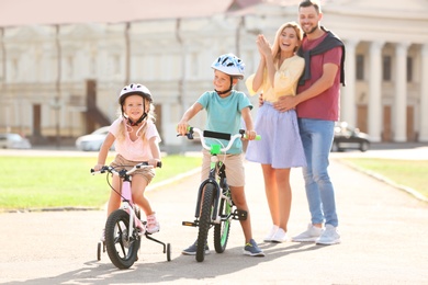 Happy parents teaching children to ride bicycles outdoors