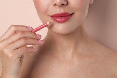 Photo of Young woman with beautiful pink lip pencil on light background, closeup