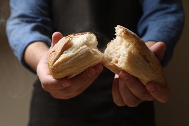 Photo of Man breaking loaf of fresh bread on dark background, closeup
